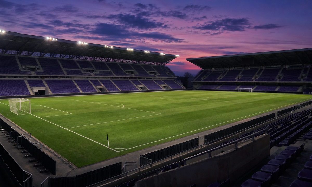 Fiorentina in tv - stadio vuoto al tramonto con seggiolini viola e prato illuminato