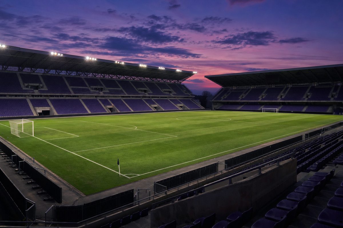 Fiorentina in tv - stadio vuoto al tramonto con seggiolini viola e prato illuminato